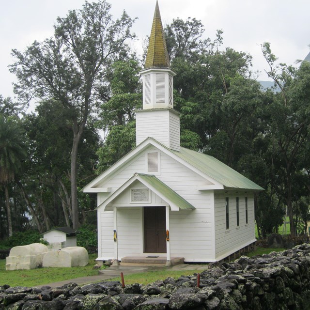 Green grass with white church and brick fence. 