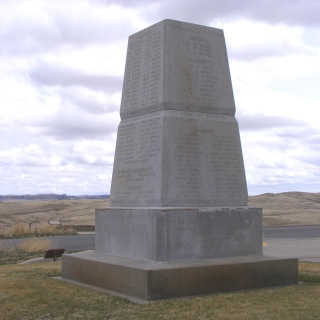 An expansive grassy field with a large stone monument NPS photo. 