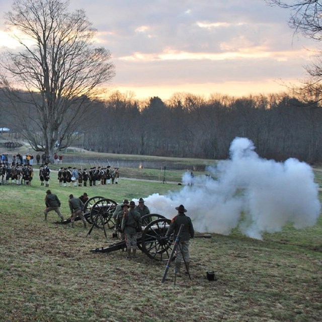 Men dressed in historical clothing firing cannons an a hillside at dusk. Courtesy NPS. 