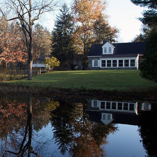 Photo of two story house with pond and vegetation in foreground. Courtesy NPS. 