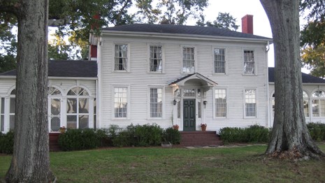 large white house with green grass in front and trees left and right