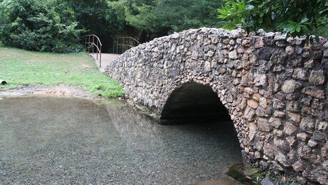 A stone bridge crosses a small meadering stream.