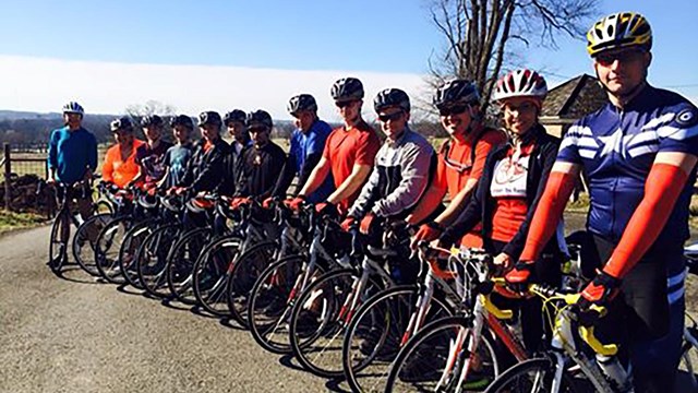 A group of people stand in a row, straddling their bicycles.