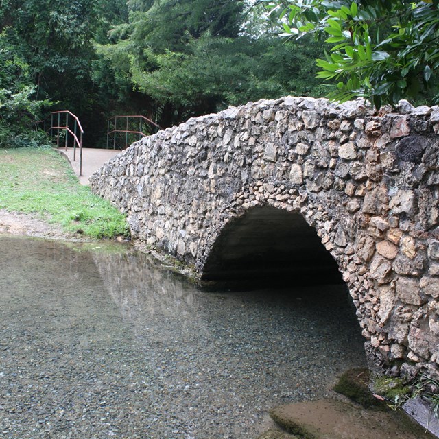 A stone bridge crosses a small meadering stream.