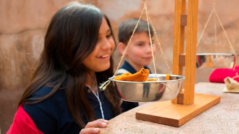 Elementary students smile in background behind balance scale.