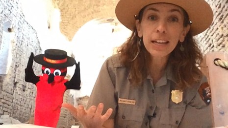ranger sitting cross-legged with book on her lap and large red bird with black hat behind