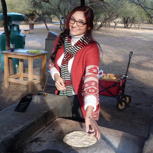 woman reaching to pick up tortilla from comal