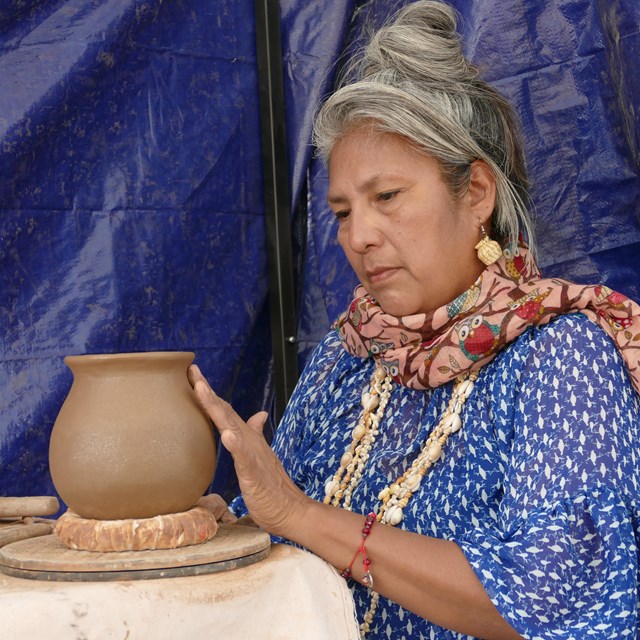 Demonstrator smoothing a ceramic pot.