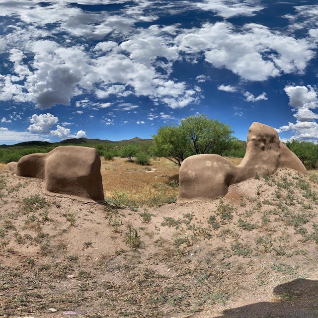 mud-coated adobe walls with hilly landscape behind and sky above