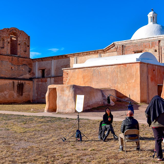 woman in interview position in front of Tumacácori church