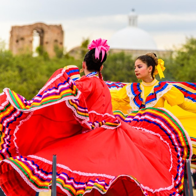 Dancers with colorful outfits moving in front of adobe church.