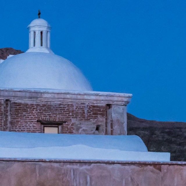 Night image of adobe church with full moon in the background.