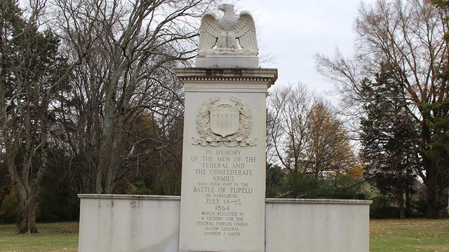 White granite monument with a carved eagle on top. Etched wording about the battle of the front
