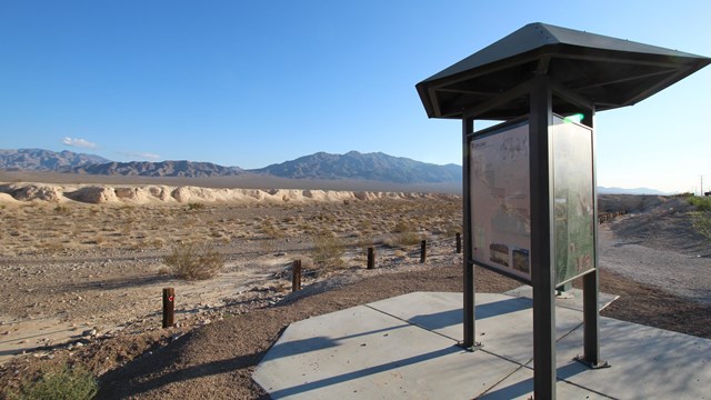 A trailhead kiosk surrounded by desert badlands and a mountain range