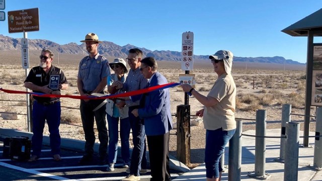 NPS ranger, volunteers, and local officials pose at a ribbon cutting at a trailhead.