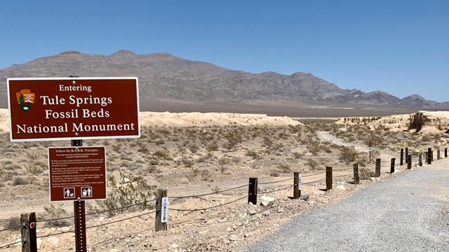 A sign "Now entering Tule Springs Fossil Beds National Monument" at a trailhead and desert landscape