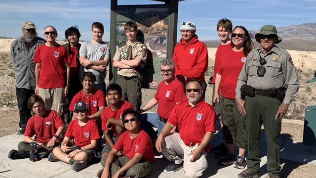 A group of eagle scouts pose with a park ranger and exhibit kiosk.