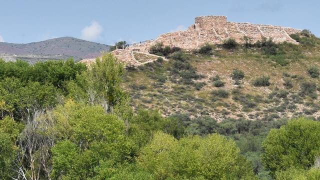 a small hill topped with stone walls stands above green bushes