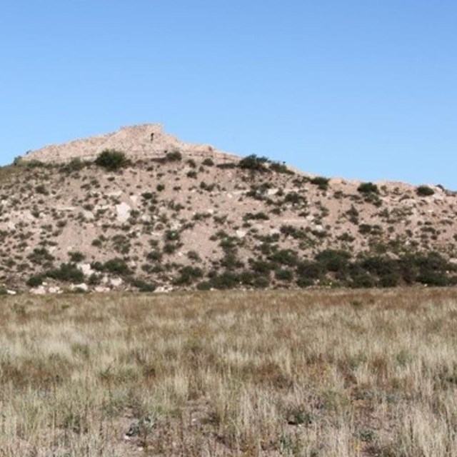 an old stone pueblo at the top of a hill, with a flat meadow in the foreground
