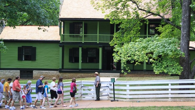 Park Ranger leading a group of people towards a green two-story frame house.