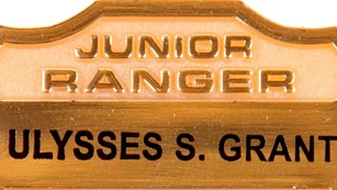 Gold Junior Ranger Badge with black text. 