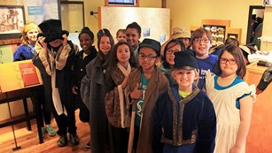 Group of students wearing costumes with historic clothing inside a museum. 