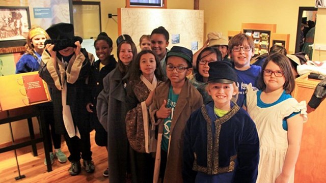 Group of students wearing costumes with historic clothing inside a museum. 