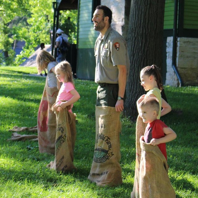 Park Ranger and children in an open field lined up for a sack race.