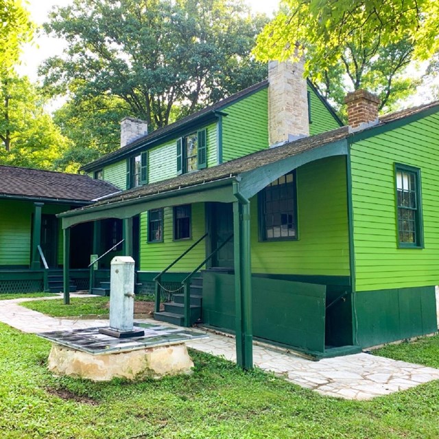 Green house with sistern pump in foreground and trees in background.