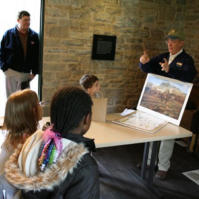 Man standing inside a stone building giving a presentation to an audience. 