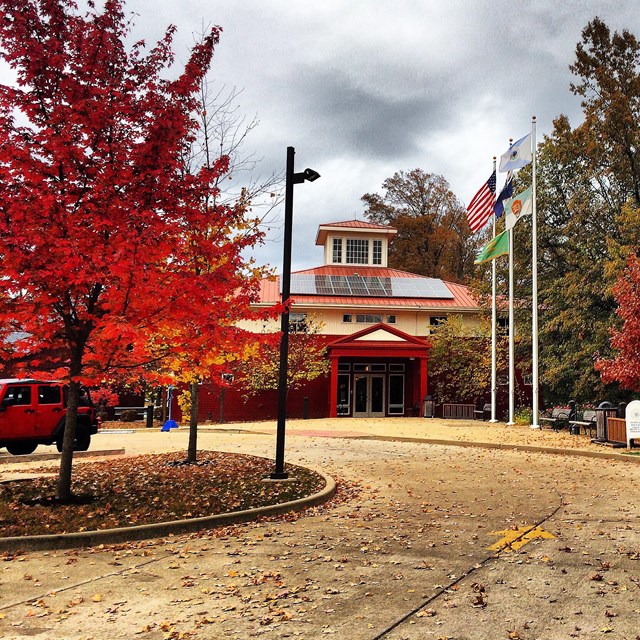 Red and white building with solar panels on the roof & multicolored trees surrounding the building.