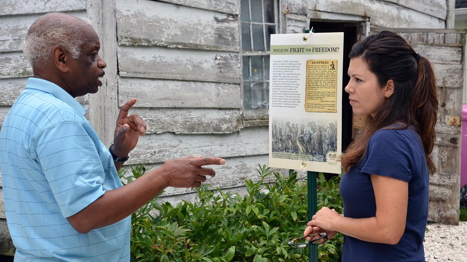 Two people stand in front of a run down building and discuss the history of the Underground Railroad