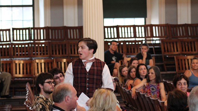 Photograph of a person in period costume speaking to a crowd of people