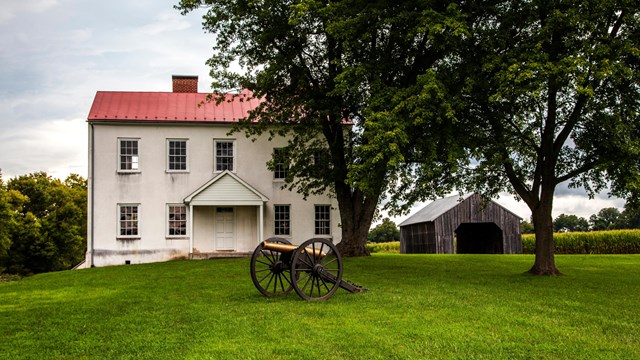 White building with red tin roof. Cannon sits in the front lawn.