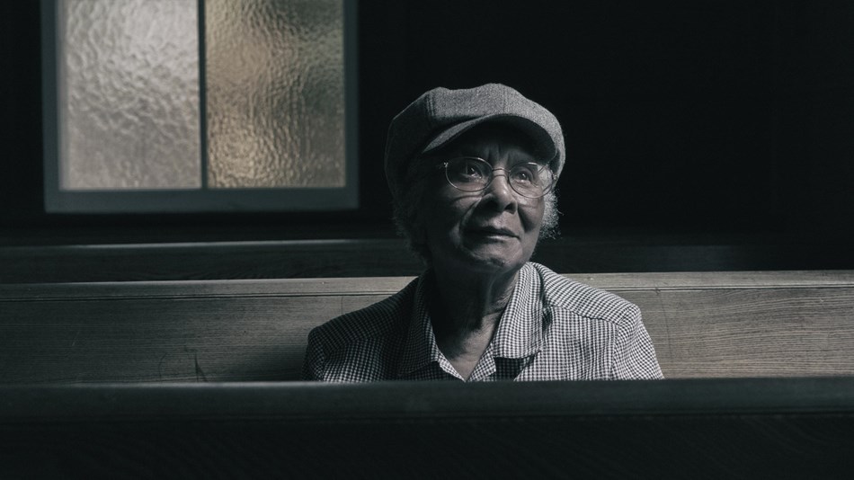 A woman sits in a wooden church pew as light cascades on her face.