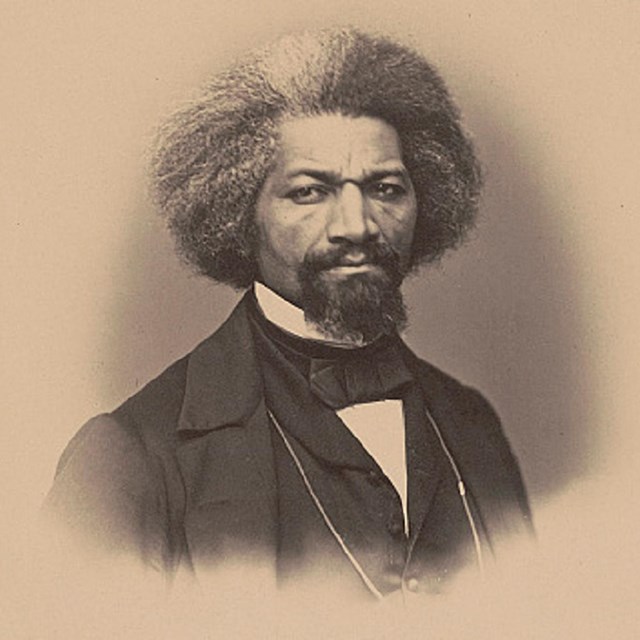 Image of Frederick Douglass wearing a suit and staring directly towards the viewer.