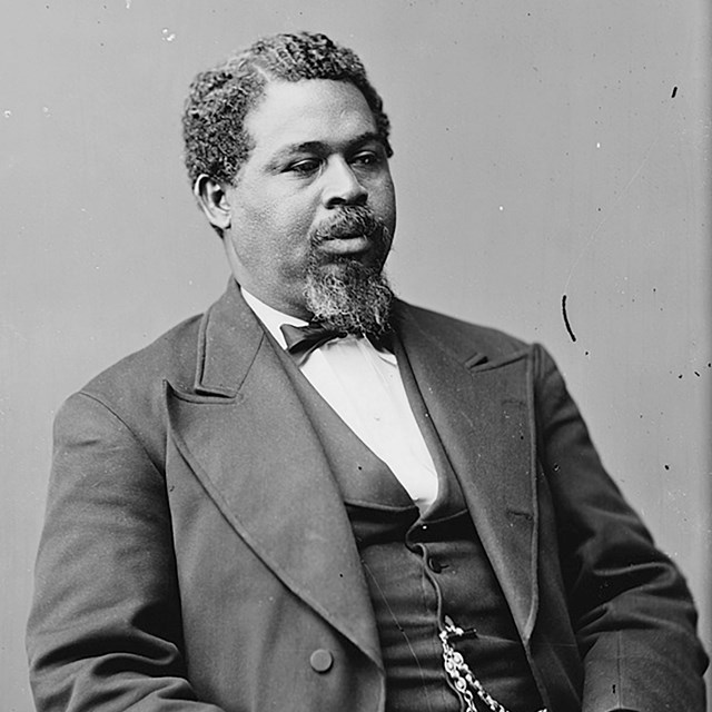 Photograph of Black man sitting at three quarter profile in a suit.