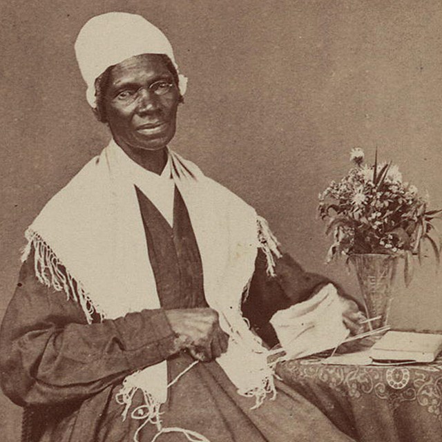 Sojourner Truth sits at a table with sewing materials.