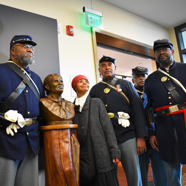 An actor dressed as Harriet Tubman and actors dressed as soldiers stand around a Harriet Tubman bust