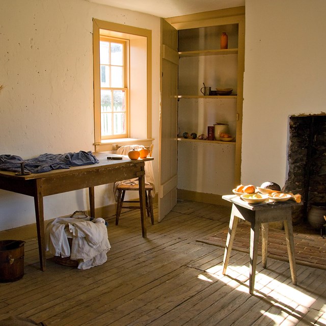 Inside slave quarters. A plain room has a table, chair, and a broom, with a small window.