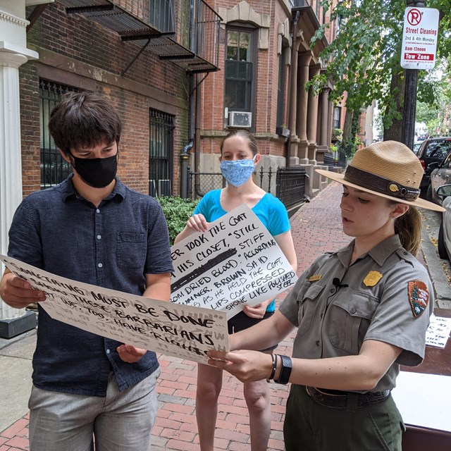 A white man and white woman hold cue cards for a ranger to explain what they mean.