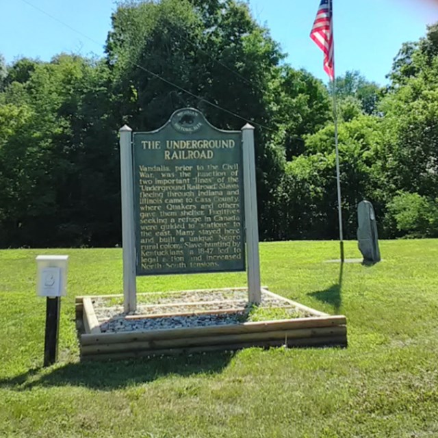 Image of an Underground Railroad sign and American Flag on a grassy area.