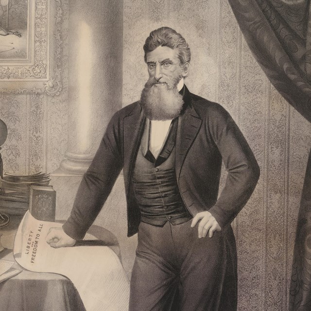 John Brown Stands in front of a table with his hand resting on a document.