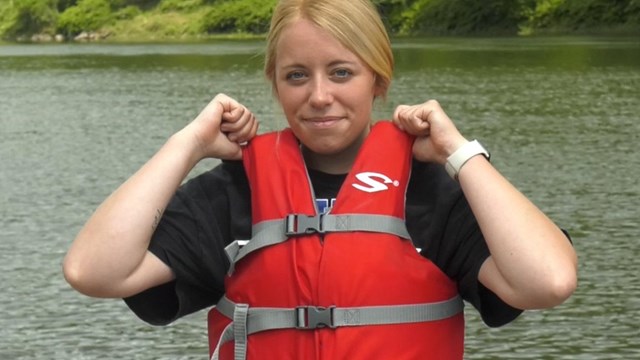 Woman wearing life jacket buckled snugly closed. She tugs on shoulders but it doesn't give.