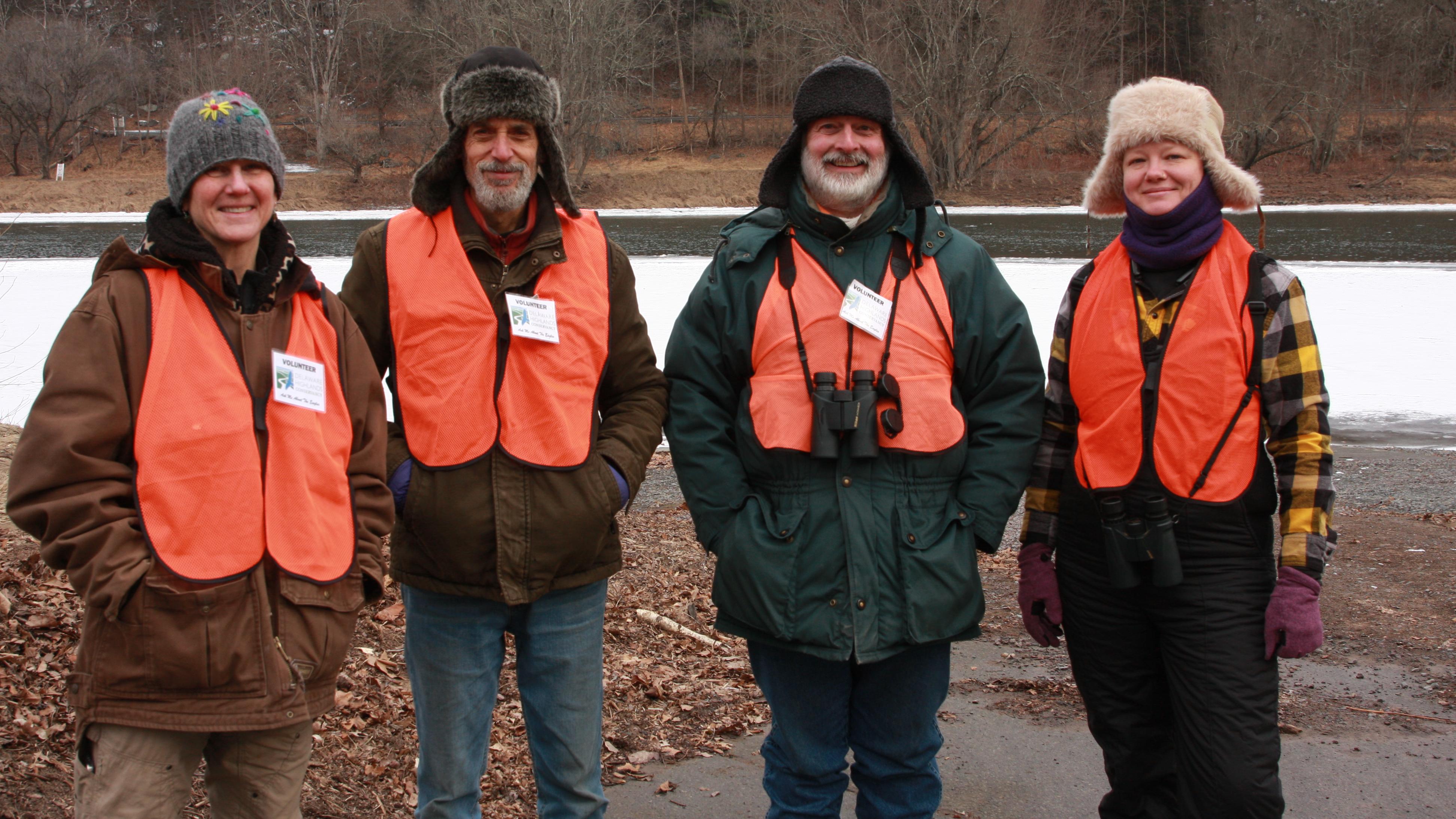 Four volunteers in thick winter clothing smiling in front of frozen river.