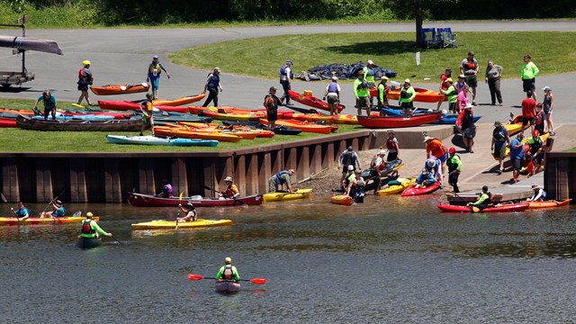 Public access area into a river. Paved ramp inclines into the river. People with kayaks enter water.