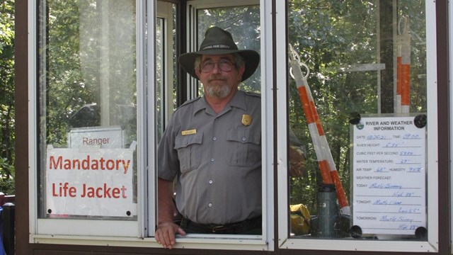 NPS information kiosk on wheels with park ranger inside, behind glass window.