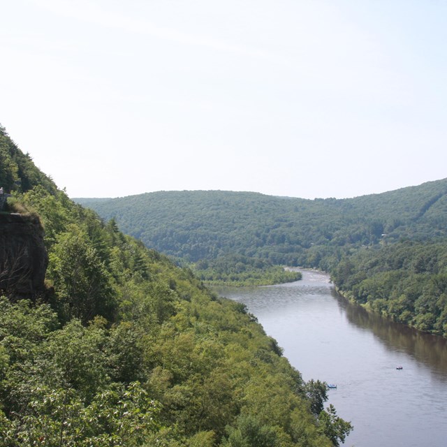 View of lush, green river valley and river from view on a side of mountain. Part of road visible.