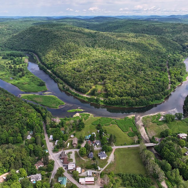 Aerial view of river valley community: buildings among trees along a river. Two bridges cross river