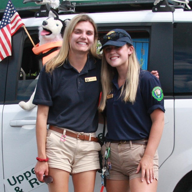 Two girls smiling together, wearing shirts with volunteer logo.